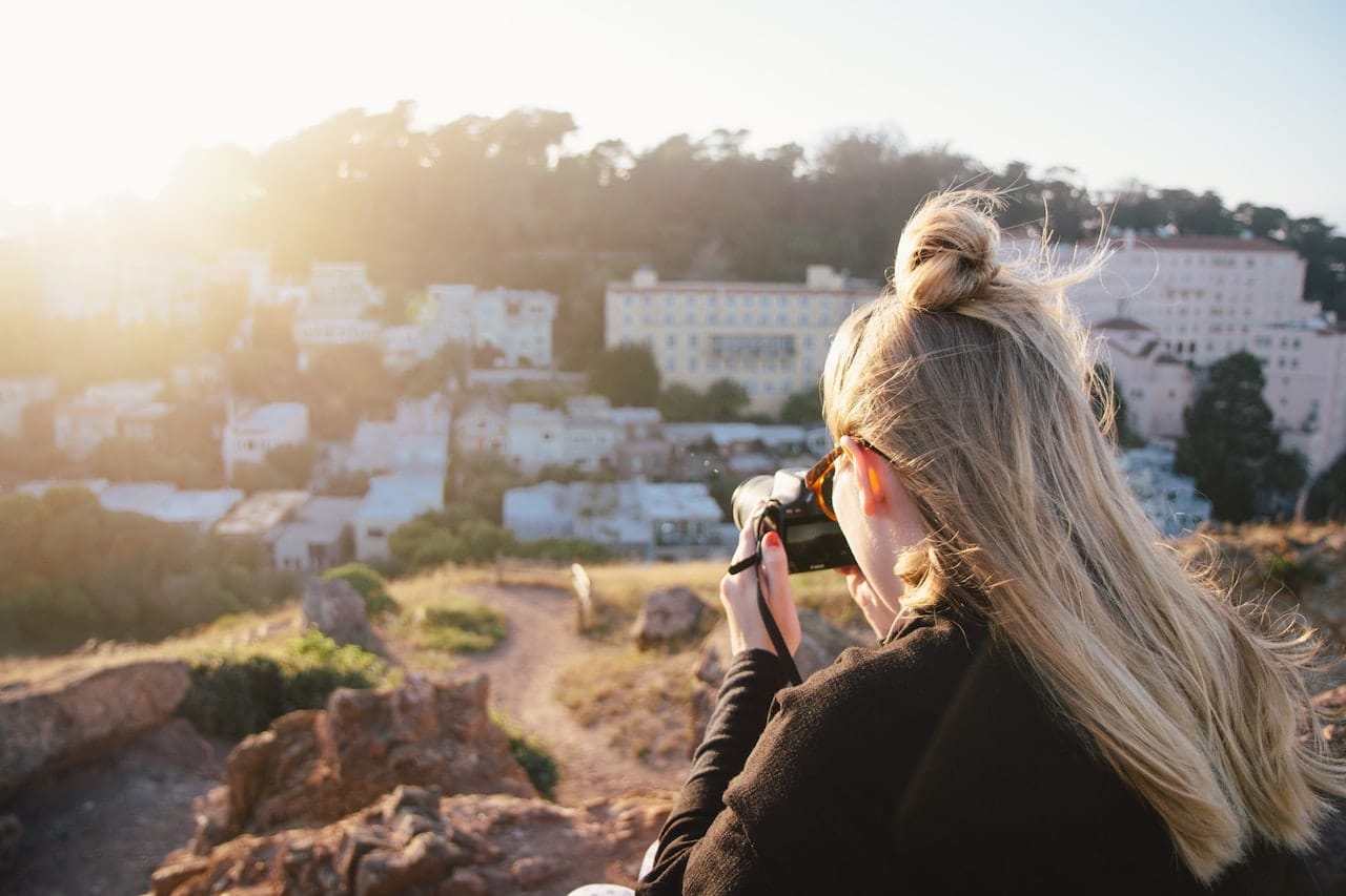 Woman in black jacket taking photo of city during daytime